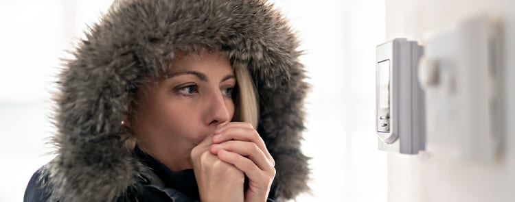 woman freezing cold blowing warm air into her hands while staring at thermostat