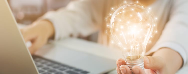 woman on laptop holding a lit up lightbulb emphasizing savings