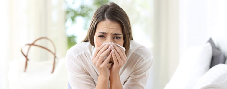 woman suffering from allergies blowing her nose