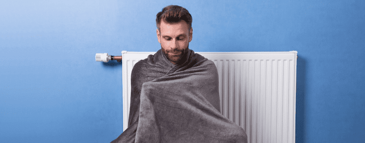 man covered up with blanket to keep warm near radiator